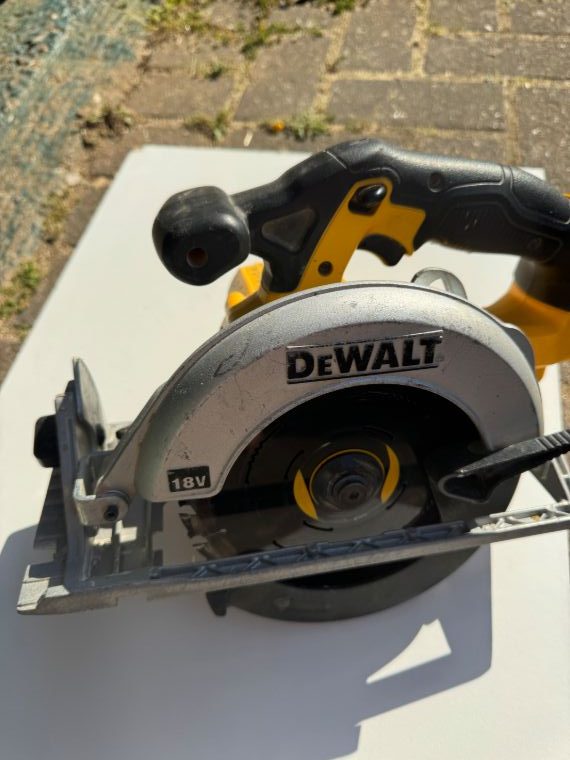 A DeWalt circular saw photographed in poor conditions — only the brand name is visible, part of the tool is out of frame, and there are heavy shadows.