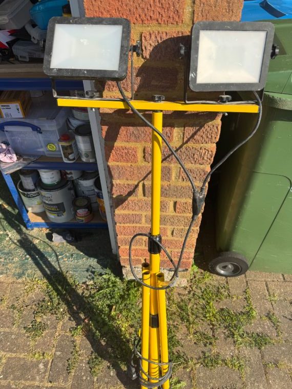A work light photographed outdoors with bins, paint tins and other clutter in the background, and no rating label in view.